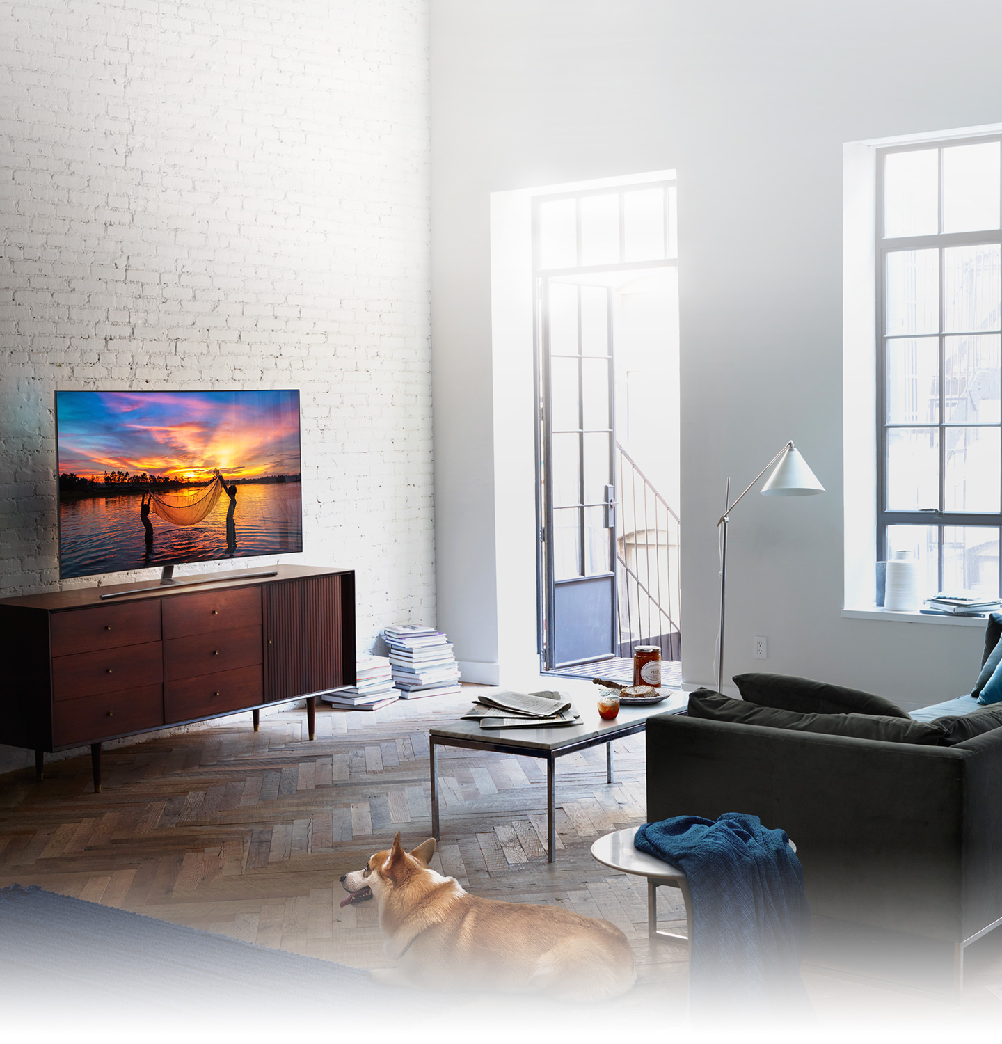 QLED TV has been set in the living room where the morning sun shines brightly and on its display shows children fishing with their net in the seashore glowing with the setting sun.