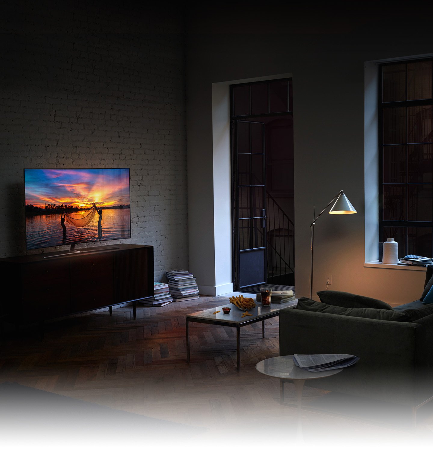 QLED TV has been set in the living room in the early evening and on its display shows children fishing with their net in the seashore glowing with the setting sun like a movie.